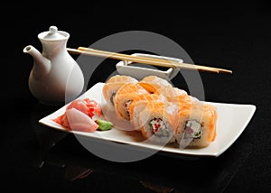 Sushi and rolls on a square plate with wasabi, soy sauce and chopsticks on a black background