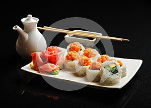 Sushi and rolls on a square plate with wasabi, soy sauce and chopsticks on a black background