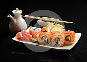 Sushi and rolls on a square plate with wasabi, soy sauce and chopsticks on a black background