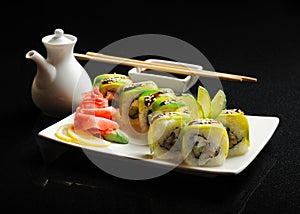 Sushi and rolls on a square plate with wasabi, soy sauce and chopsticks on a black background