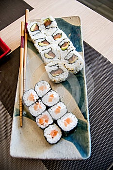 Sushi with salmon, avocado and tuna fish on a plate with chopsticks