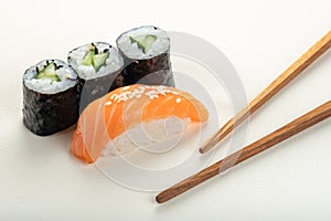 Sushi with salmon and cucumber roll with chopsticks on a light beige background