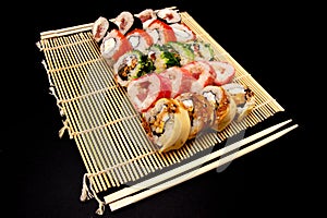 Sushi set with different maki - hosomaki, futomaki and uramaki on bamboo mate with chopsticks on a black background