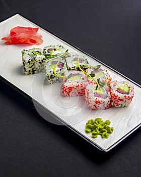 Sushi set, sushi rolls with cream cheese and caviar served on a white plate over black background