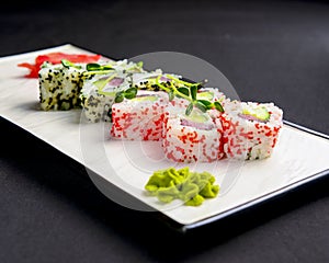 Sushi set, sushi rolls with cream cheese and caviar served on a white plate over black background