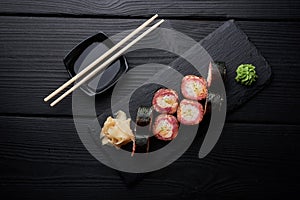 Sushi set with salmon served on black clay plate with soy sauce and chopsticks, top view. Delicious traditional Japanese food with