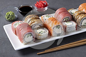Sushi set with salmon, tuna and smoked eel with philadelphia cheese on white plate on dark gray background. Served with soy sauce