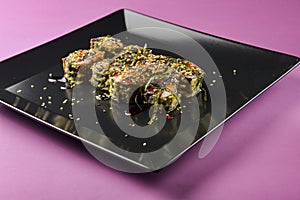 Sushi set served on a black square plate over bright pink background. Traditional Japanese cuisine, sushi rolls close up