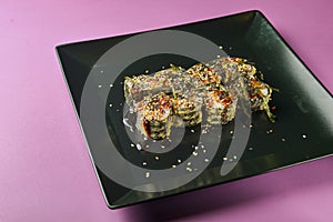 Sushi set served on a black square plate over bright pink background. Traditional Japanese cuisine, sushi rolls close up