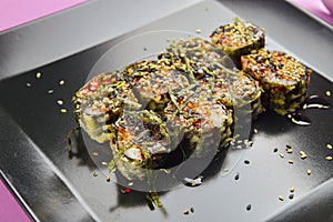 Sushi set served on a black square plate over bright pink background. Traditional Japanese cuisine, sushi rolls close up