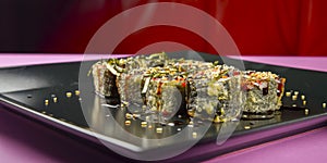 Sushi set served on a black square plate over bright pink background. Traditional Japanese cuisine, sushi rolls close up