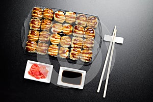 Sushi set served on a stone slate on a dark background. Sushi rolls baked with sesame seeds, unagi sauce, ginger and chopsticks.
