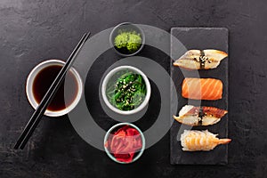 Sushi set on a slate board, soy sauce in a bowl, seaweed and ginger on the side.