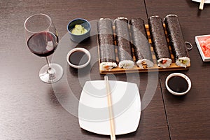 sushi set with sauce,wooden sticks and glass of wine on the brown table