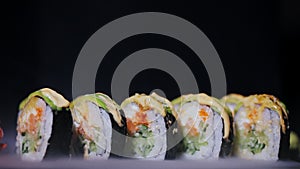Sushi with slices of salmon and fresh cucumbers. Appetizing sushi on a black stone board. Close-up