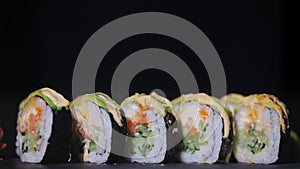 Sushi with slices of salmon and fresh cucumbers. Appetizing sushi on a black stone board. Close-up