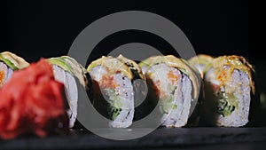 Sushi with slices of salmon and fresh cucumbers. Appetizing sushi on a black stone board. Close-up