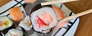 Sushi sticks in hands and set of rolls on plate. Delicious sushi with sliced rice and fresh vegetables