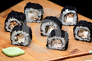 Sushi zuko maki with shrimp, cheese, cucumber, and black masago caviar. Sushi prepared for eating on a wooden board.