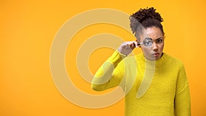 Suspecting afro-american woman looking thorough magnifying glass, inspection