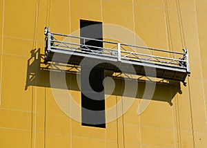 Suspended access cradle against yellow building facade