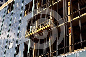 Suspended construction craddle for glazing a facade of a commercial property at sunset. Engineering urban background