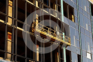 Suspended construction craddle near wall of hightower building with insulation and ventilated facade on construction site.