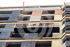 Suspended construction craddle near wall of hightower residentaial building with insulation and ventilated facade on