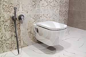 Suspended toilet and hygienic shower in interior decorated with beautiful tiles with floral pattern and marble floor