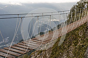 Suspended wooden bridge hanging over an abyss in mountain canyon and clouds, Extreme hike at altitude, Trekking in the mountains