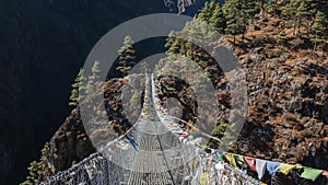 Suspension bridge with colorful flags flying in the wind, on top of a mountain range