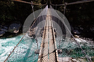 Suspension bridge over a beautiful turquoise river on the Hollyford Road, Fiordland National Park, New Zealand