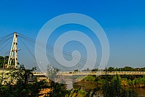 Suspension bridge spanning across Nan river to Phichit railway station in Muang district of Phichit province with blue sky and sun
