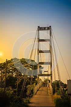 Suspension bridge spanning across Nan river to Phichit railway station in Muang district of Phichit province with blue sky and sun