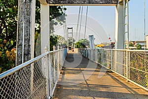 Suspension bridge spanning across Nan river to Phichit railway station in Muang district of Phichit province with blue sky and sun