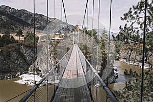 Suspension hanging bridge above water mountain river stream covered with ice snow on the background of rock island