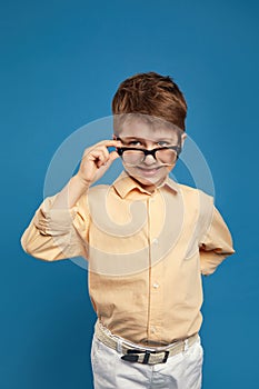 Suspicion little kid boy in beige shirt with curiosity looking through glasses at camera