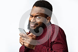 Suspicious Black Man Using Smartphone Looking At Camera, White Background.