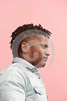 The suspicious business Afro-American man standing and suspiciously looking against pink background. Profile view.