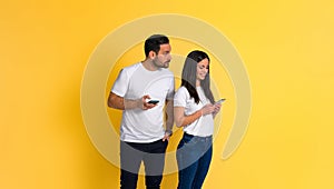 Suspicious and possessive boyfriend with mobile phone spying on smiling girlfriend chatting on social media using smartphone while photo