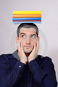 Suspicious student holding a pile of books on his head raising his eyebrow.