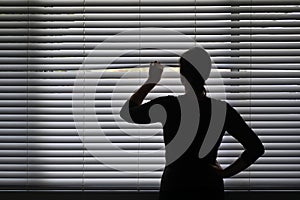 Suspicious woman looking outside through a venetian curtain blinds