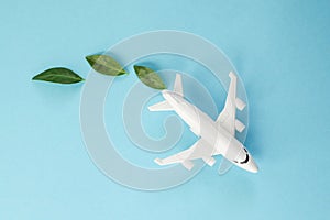 Sustainable Aviation Fuel. White airplane model, fresh green leaves on blue background. Green Biofuel for aviation photo
