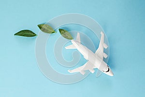 Sustainable Aviation Fuel. White airplane model, fresh green leaves on blue background. Green Biofuel for aviation