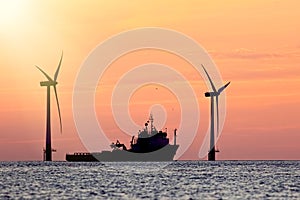 Sustainable resources. Wind farm with ship silhouette at tropical sunrise or sunset. Solar and wind energy and food supply