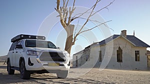 SUV 4x4 car parked near dried dead tree and Garub railroad station. Kolmanskop.