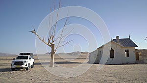 SUV 4x4 car parked near dried dead tree and Garub railroad station. Kolmanskop.