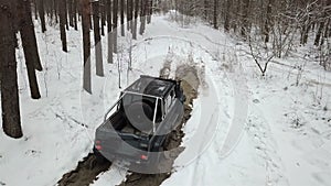 SUV 6x6 overcomes a large puddle on a dirt road in the winter forest. Off-road