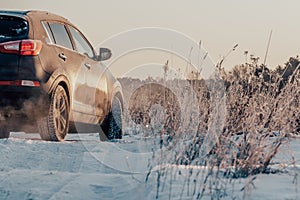 SUV car drives on snowy road in countryside in winter. Dangerous ice cover