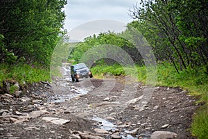 Suv car driving on a dirt off road with puddles and stones in the forest
